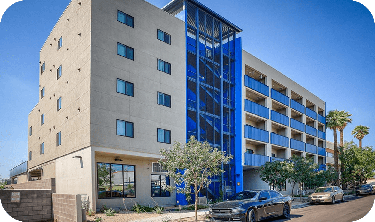 Exterior and an apartment building five stories tall with a bright blue staircase in the center.