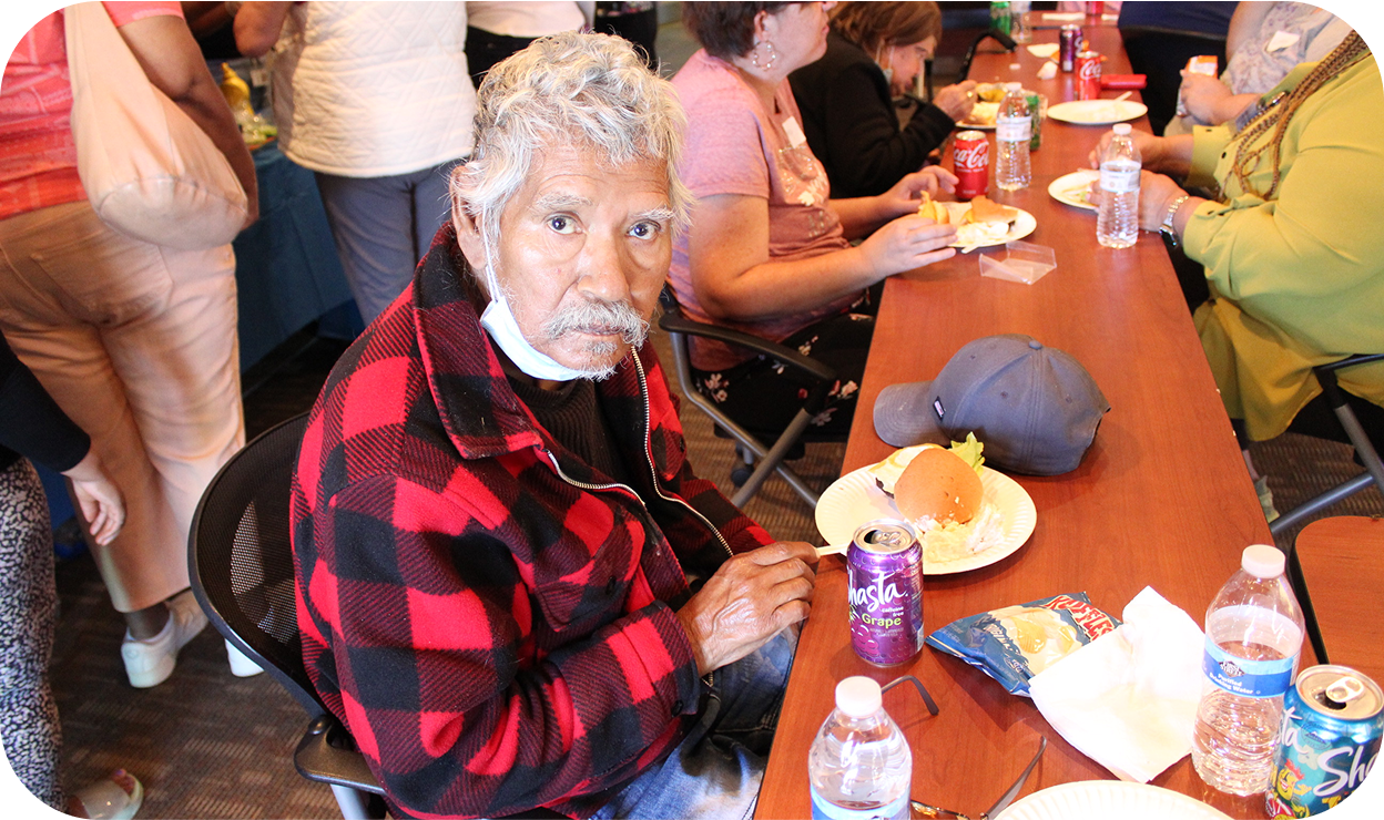 an elderly man snacking at a table with other elderly people
